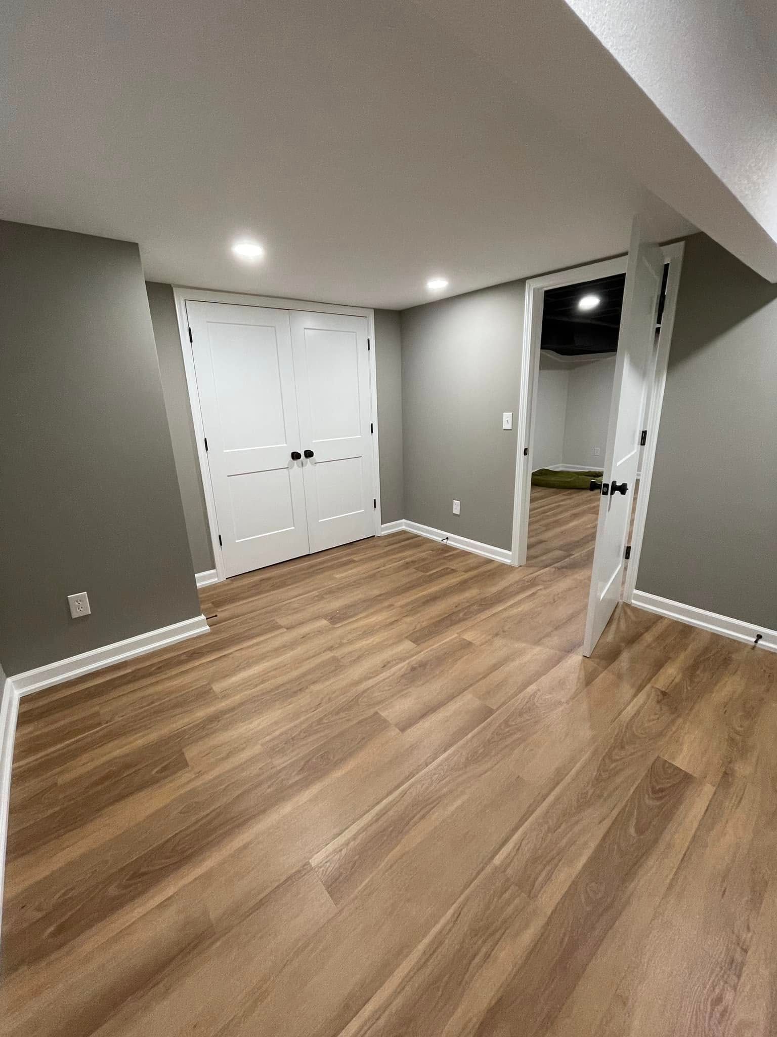 Empty gray room with wood floors, white closet doors, recessed lights, and a doorway to a darker hallway