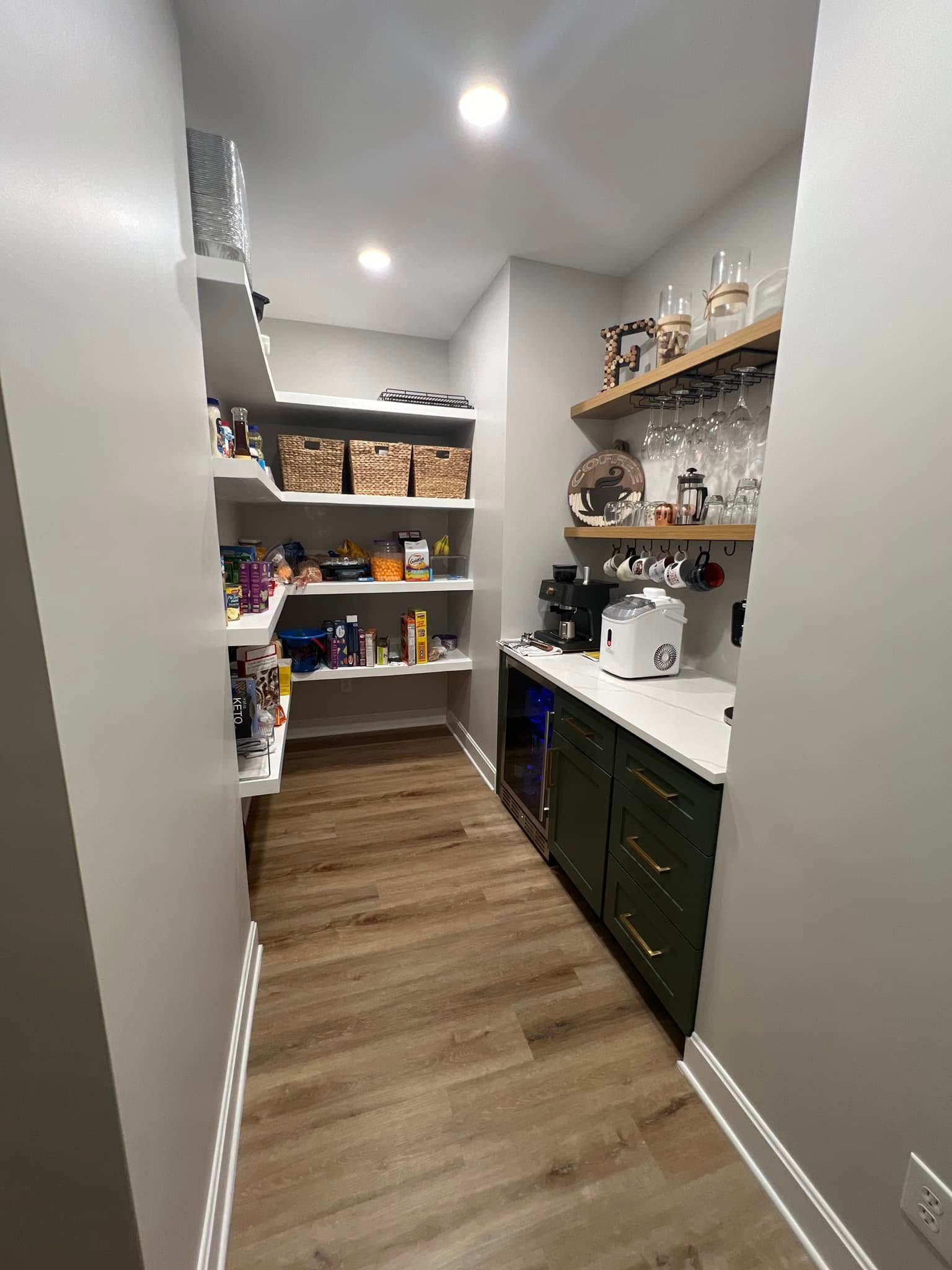 Narrow pantry with shelves of snacks and jars, white countertop, and green cabinets under recessed lighting