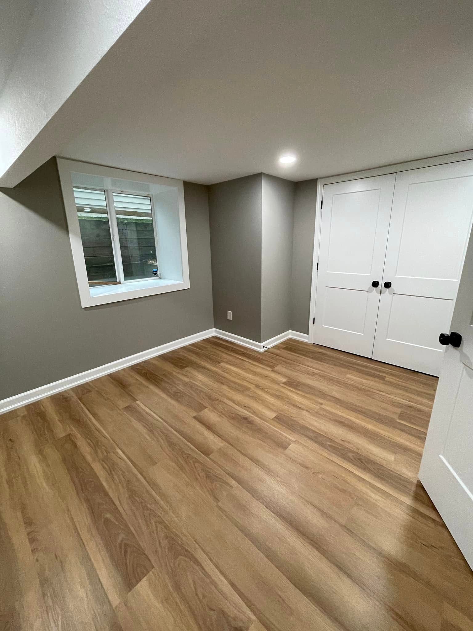 Empty modern bedroom with wood floors, gray walls, window, and white closet doors
