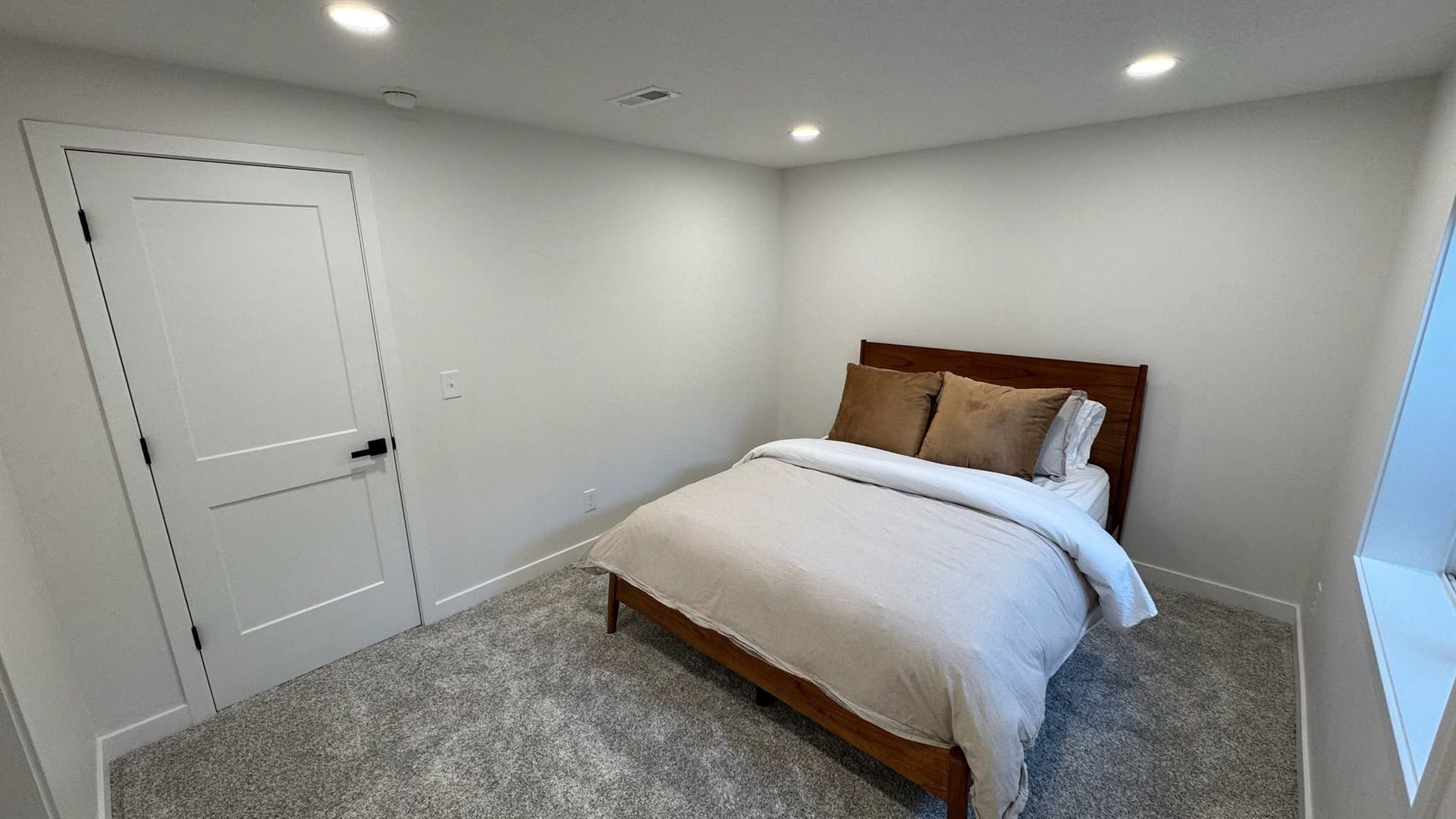 Small white bedroom with a bed, gray carpet, recessed lights, and a closed door