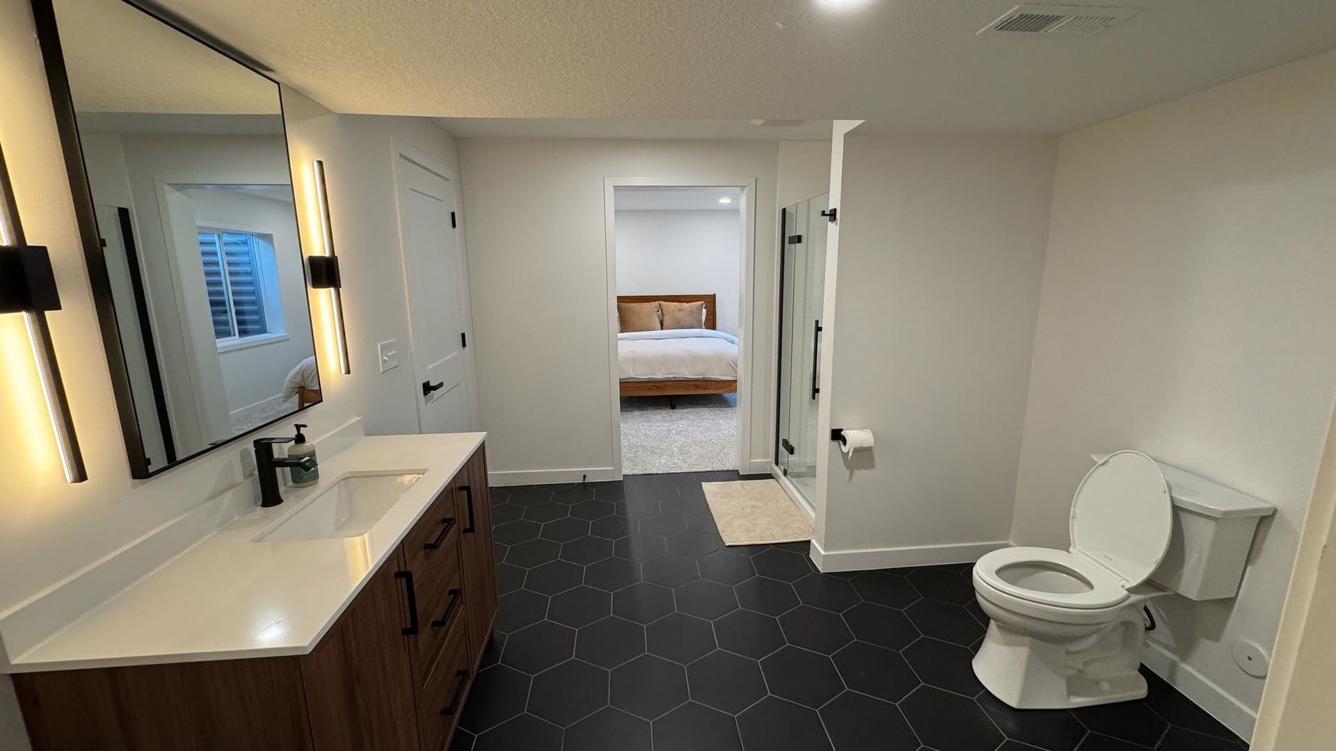 Modern accessible bathroom with vanity, toilet, and open doorway to a bedroom.