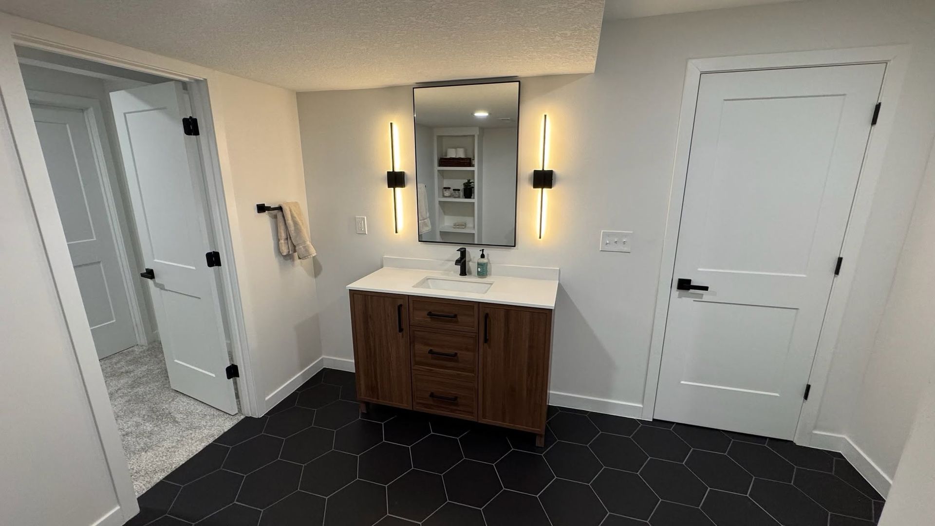 Bathroom vanity with mirror and wall sconces, white doors, and dark tile floor