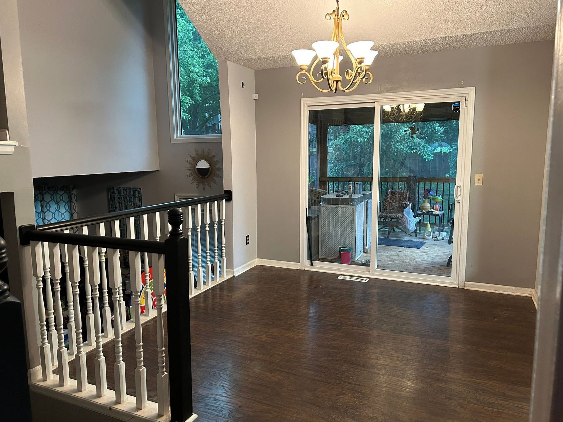 Empty dining room with dark wood floors, chandelier, and sliding glass doors to a backyard.