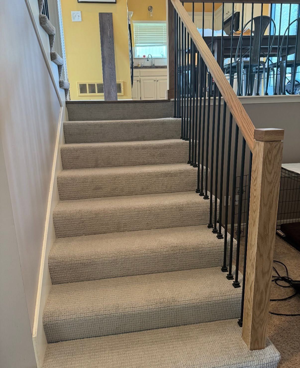 Carpeted staircase with beige walls and black railing leading to an upper landing