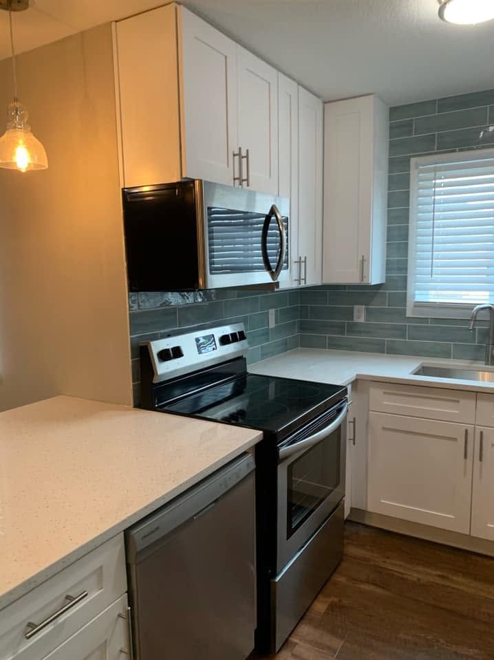 Modern white kitchen with stainless steel appliances, gray tile backsplash, and a window over the sink.