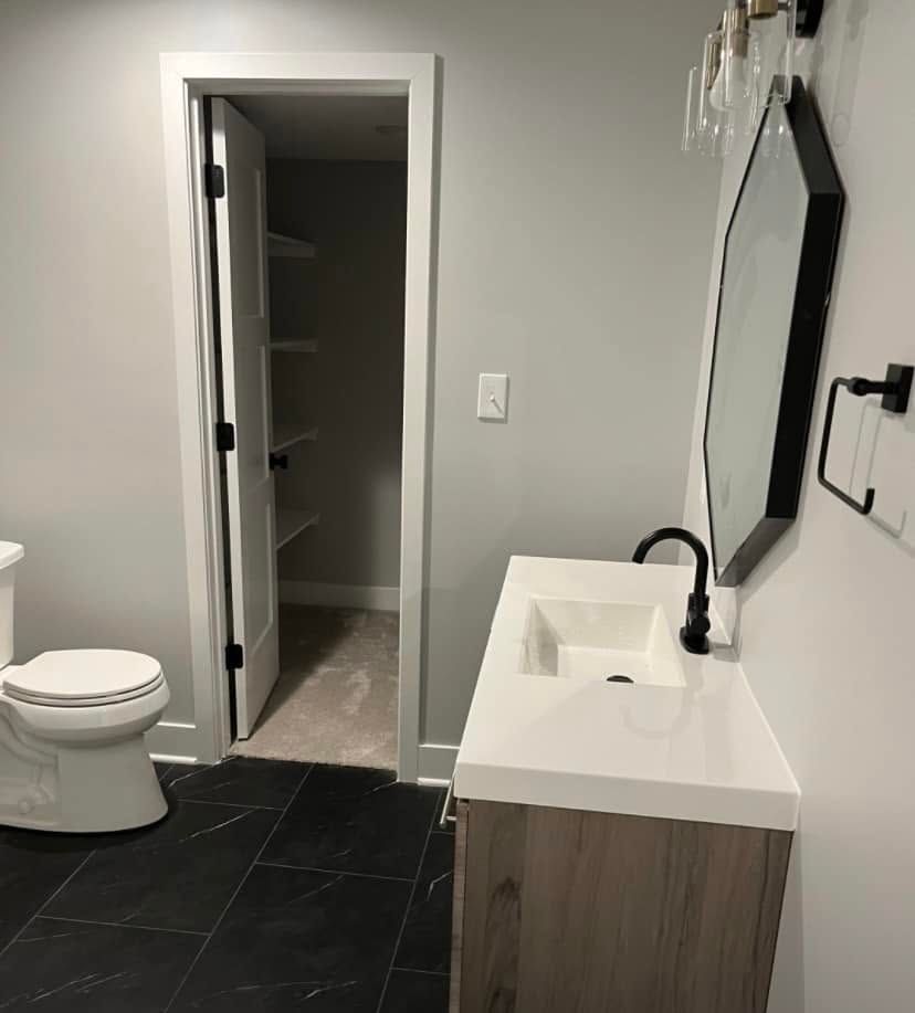 Modern bathroom with black tile floor, white toilet and vanity, and open closet door.