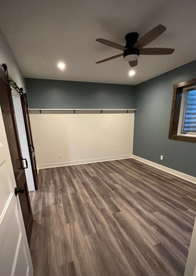 Empty bedroom with gray walls, wood-look flooring, ceiling fan, and a window with blinds.