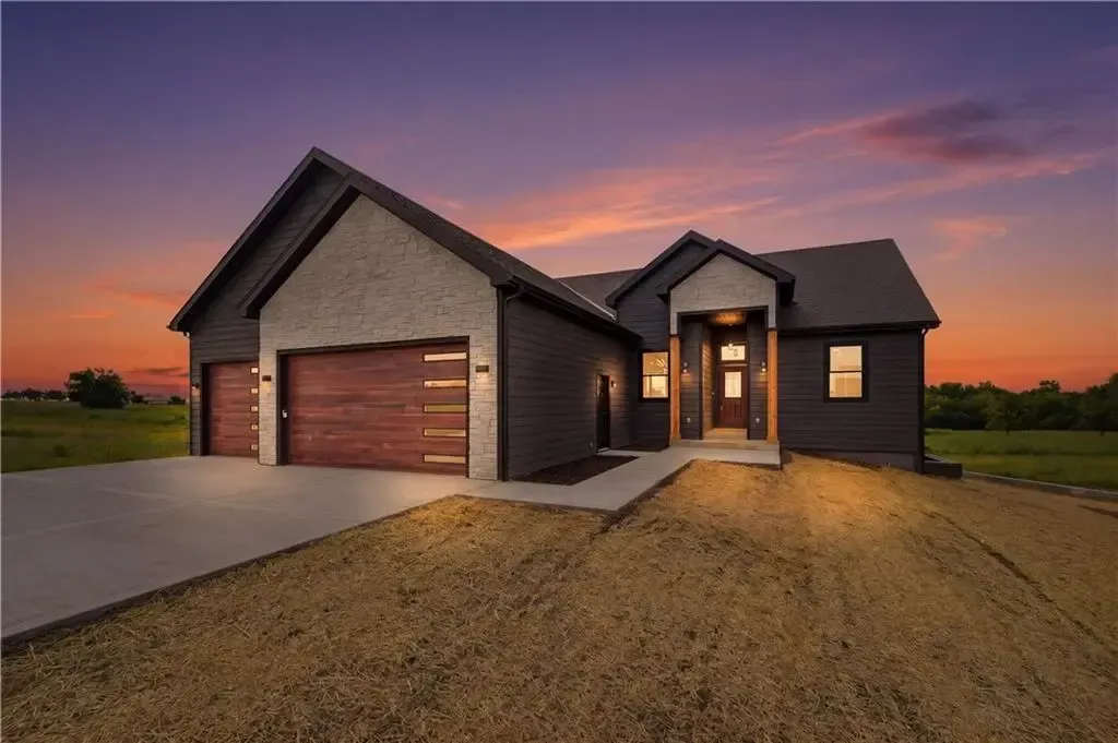Modern dark-gray house with a two-car garage at sunset, front walkway lit warmly
