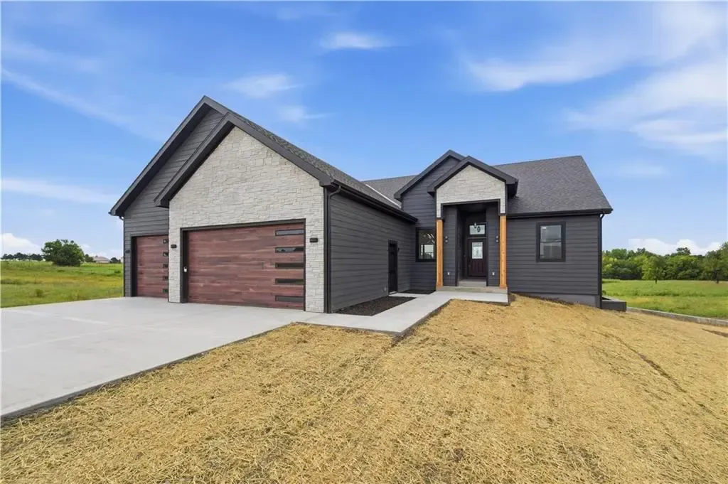 Modern gray house with two-car garage, driveway, and gravel front yard under blue sky