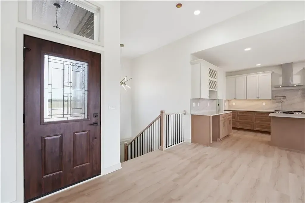 Bright entryway with dark wood front door, light flooring, and open kitchen area beyond the stairs