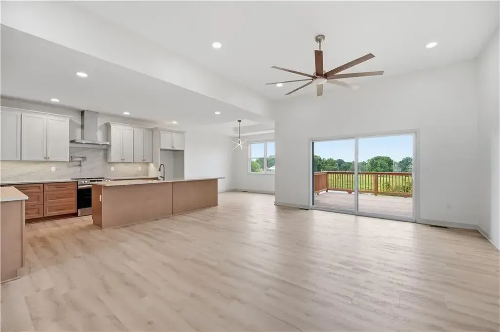 Spacious empty kitchen and living area with light wood floors, white walls, ceiling fan, and sliding glass doors to patio