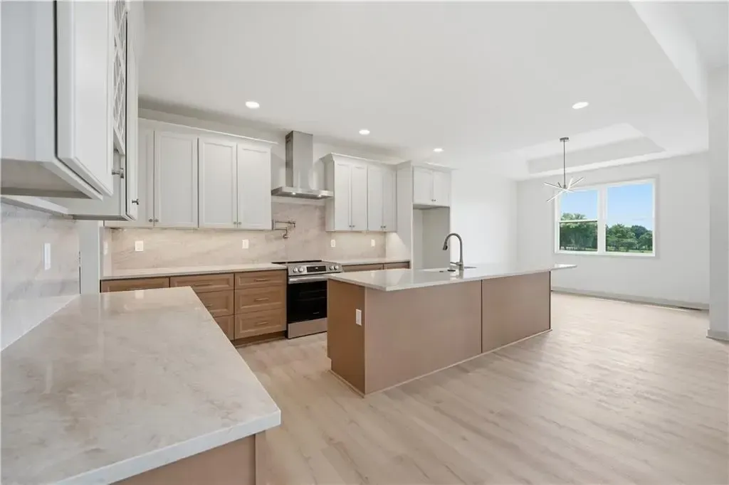 Bright modern kitchen with white cabinets, beige island, wood floors, and large windows