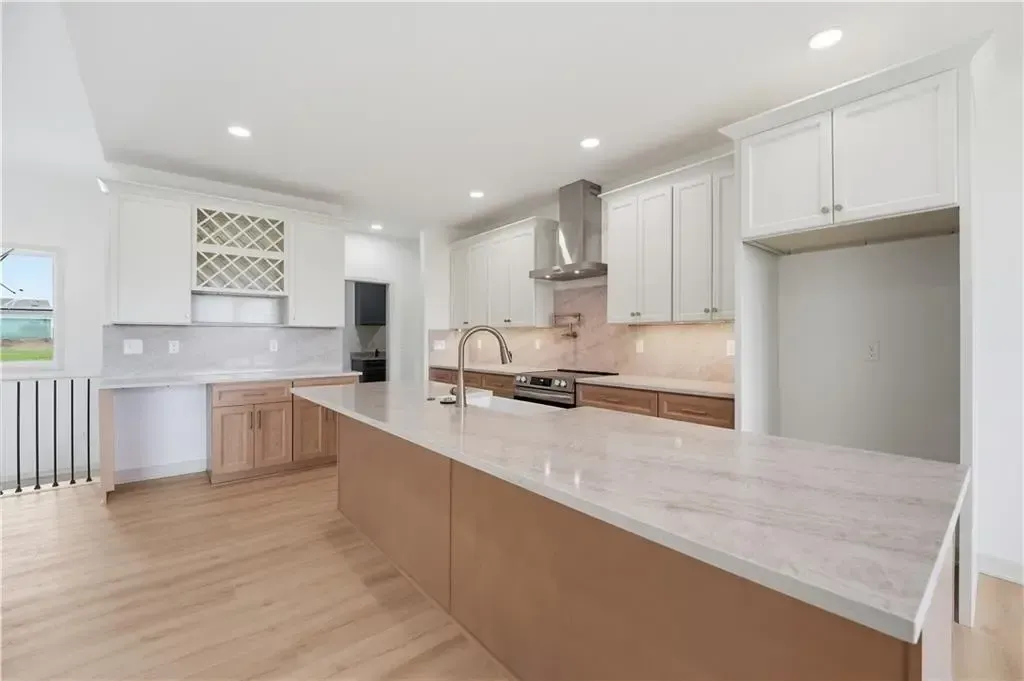 Bright modern kitchen with white cabinets, light wood floors, and a long marble island.