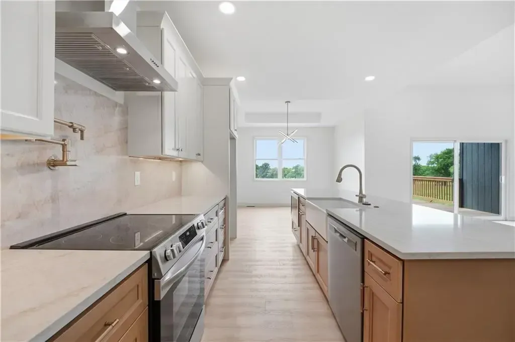 Bright modern kitchen with white cabinets, stainless stove, island sink, and large windows to the backyard