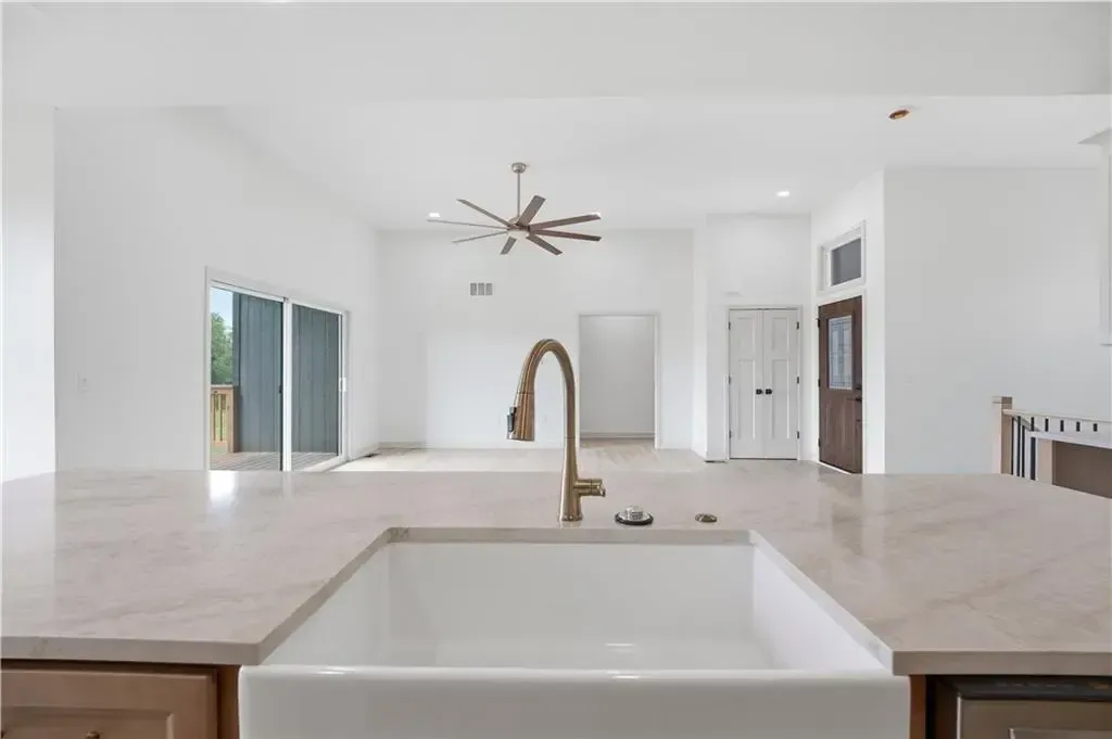 Bright modern kitchen with white island, sink faucet, ceiling fan, and sliding glass doors leading outside