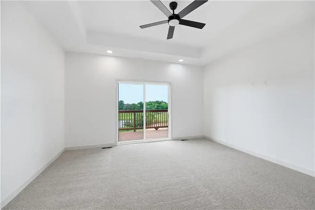Bright empty white room with ceiling fan, carpeted floor, and sliding glass doors to a balcony.