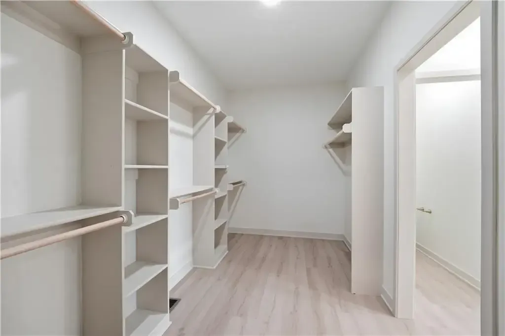 Bright empty walk-in closet with white built-in shelves and light wood flooring