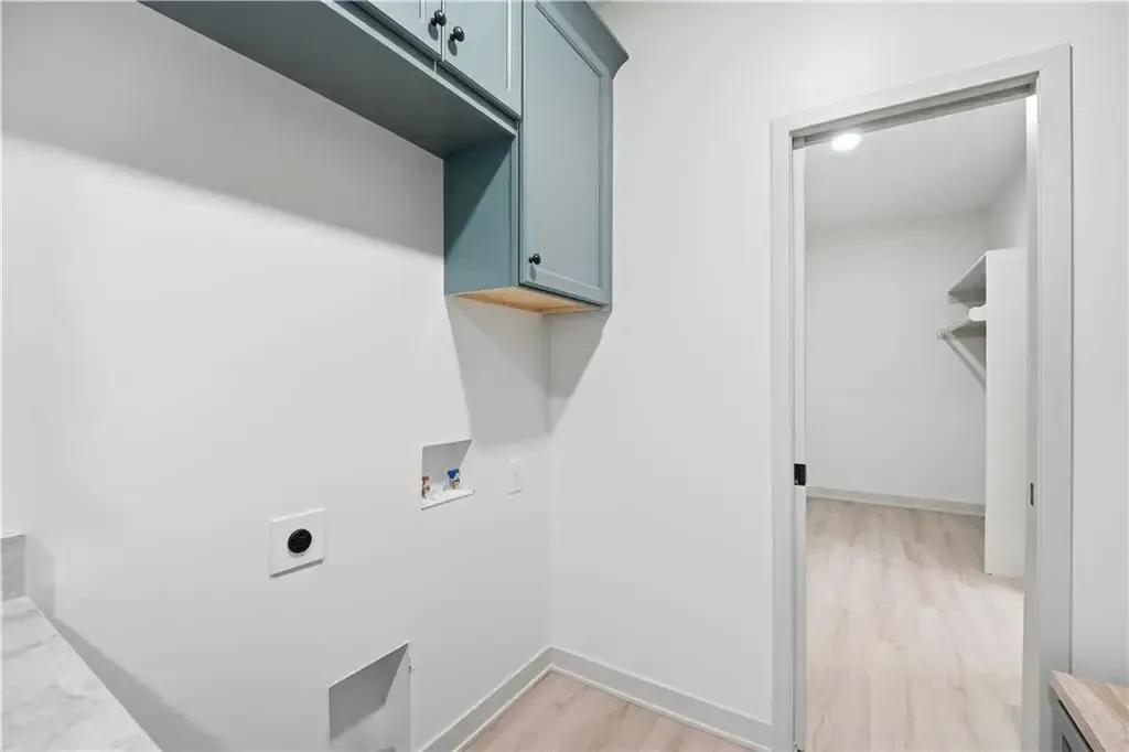 Small utility room with white walls, pale wood floor, and built-in cabinets, viewed toward an open doorway.