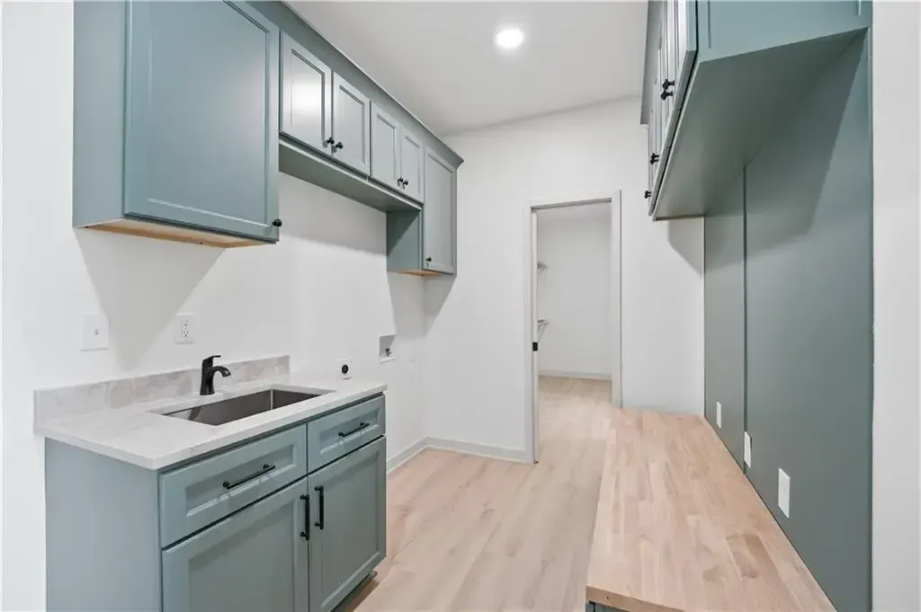 Modern laundry room with teal cabinets, white countertops, and light wood floors