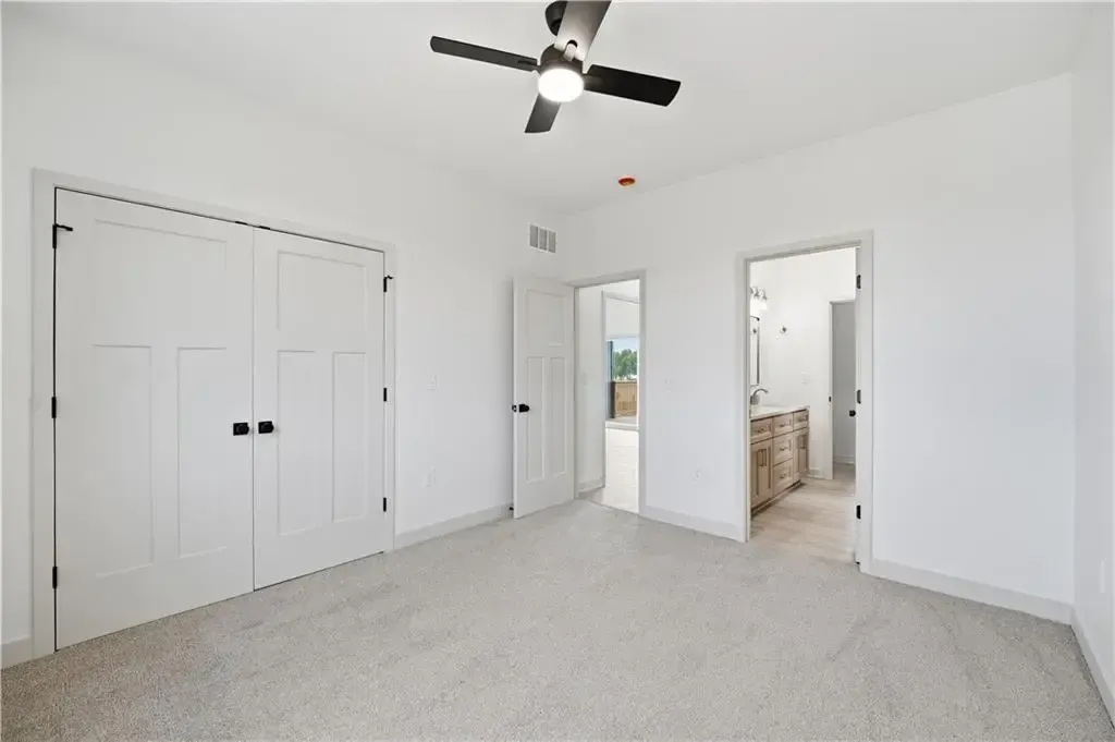 Empty white bedroom with carpet, ceiling fan, and two open doorways.