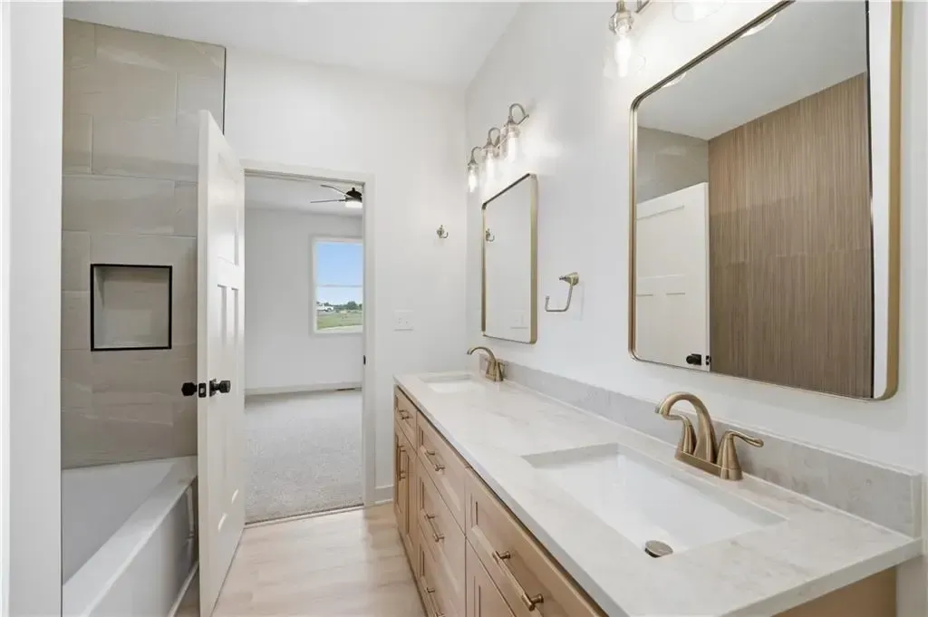 Bright modern bathroom with double vanity, large mirror, and white tile, opening to a shower area and window.