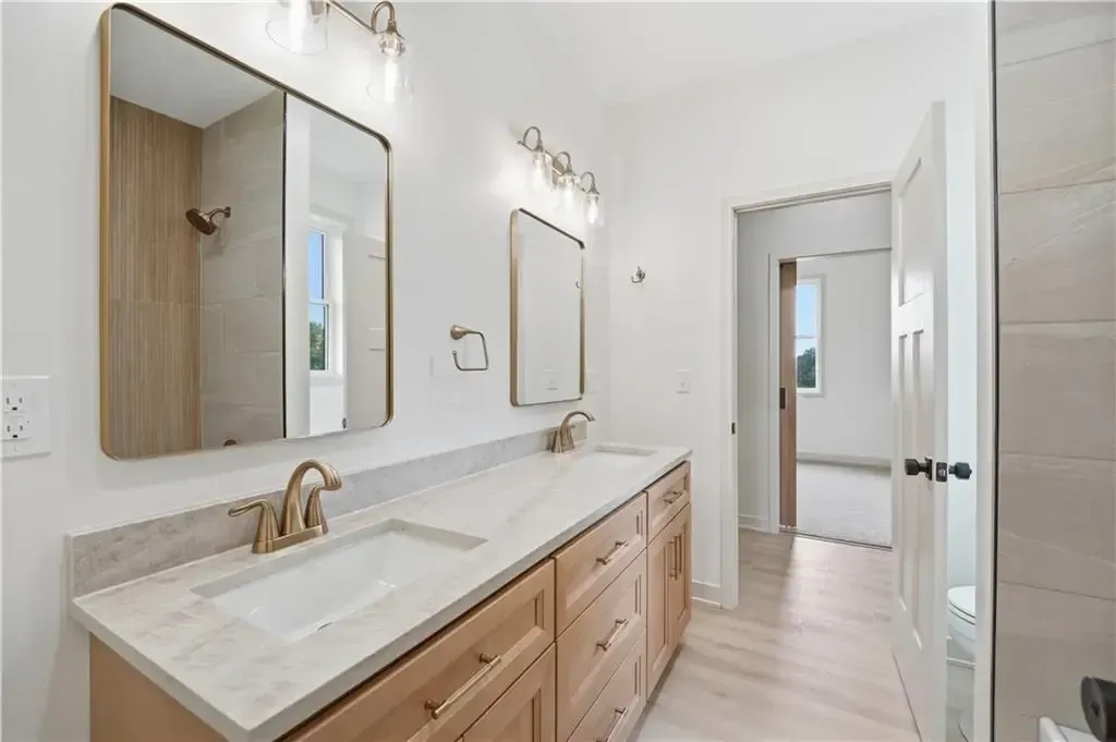 Bright bathroom with double vanity, large mirrors, light wood cabinets, and white marble counters