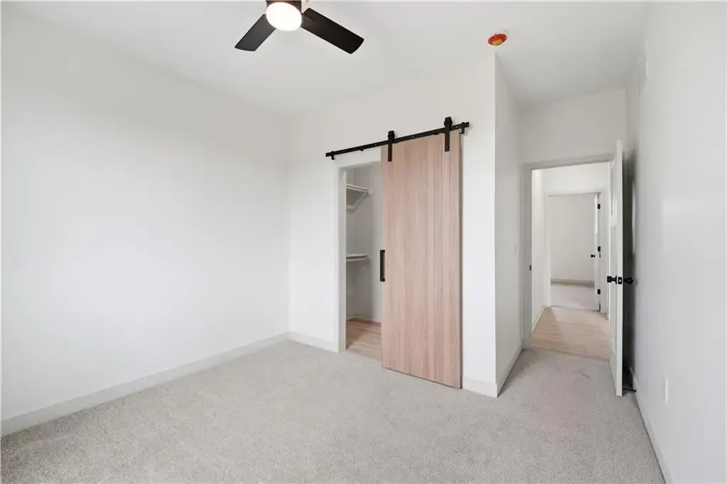 Empty white bedroom with carpet, ceiling fan, and a sliding barn door to the closet and hallway.