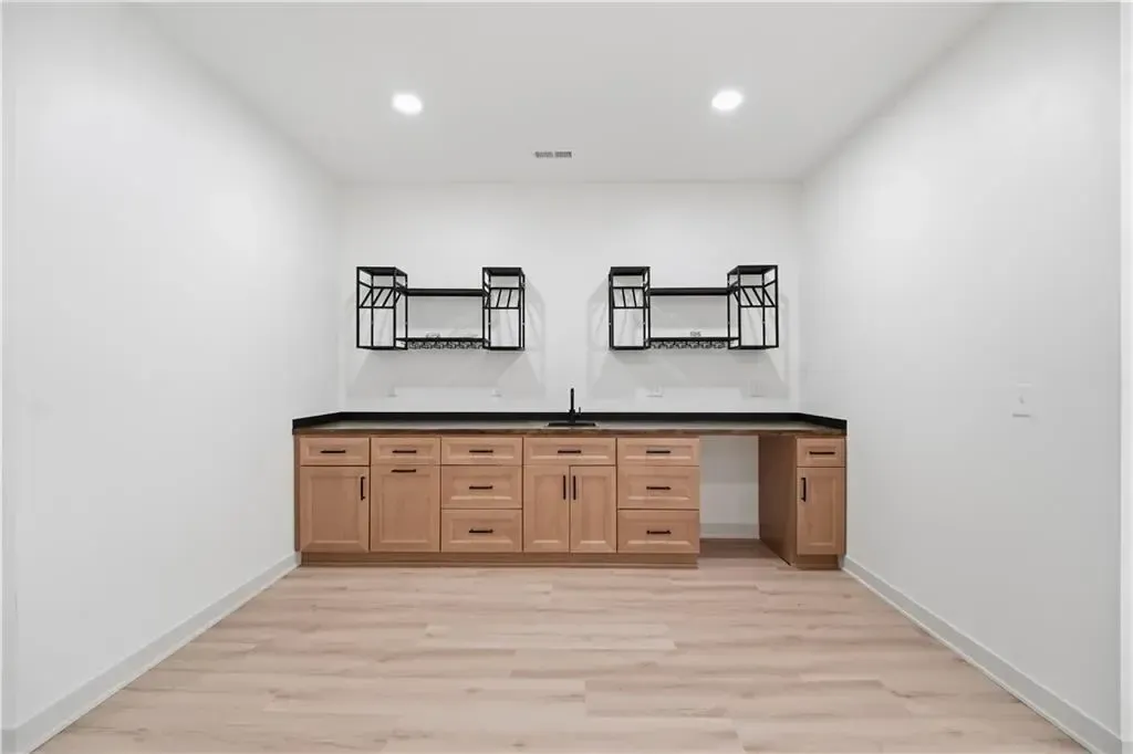 Empty white room with built-in wood desk, drawers, wall shelves, and recessed ceiling lights