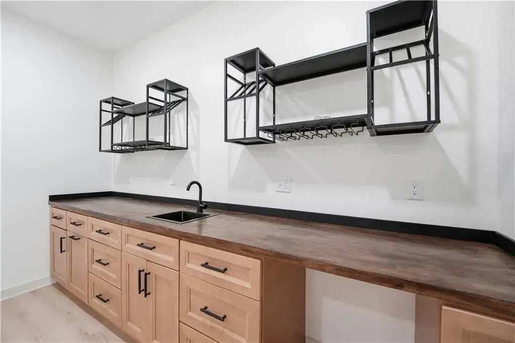 Modern kitchen with wood cabinets, dark countertop, black metal shelves, and a sink against a white wall