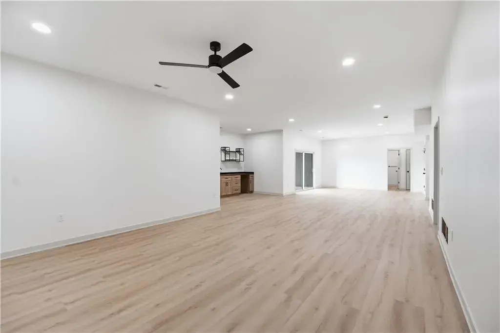 Empty modern living room with white walls, light wood floors, ceiling fan, and bright open layout