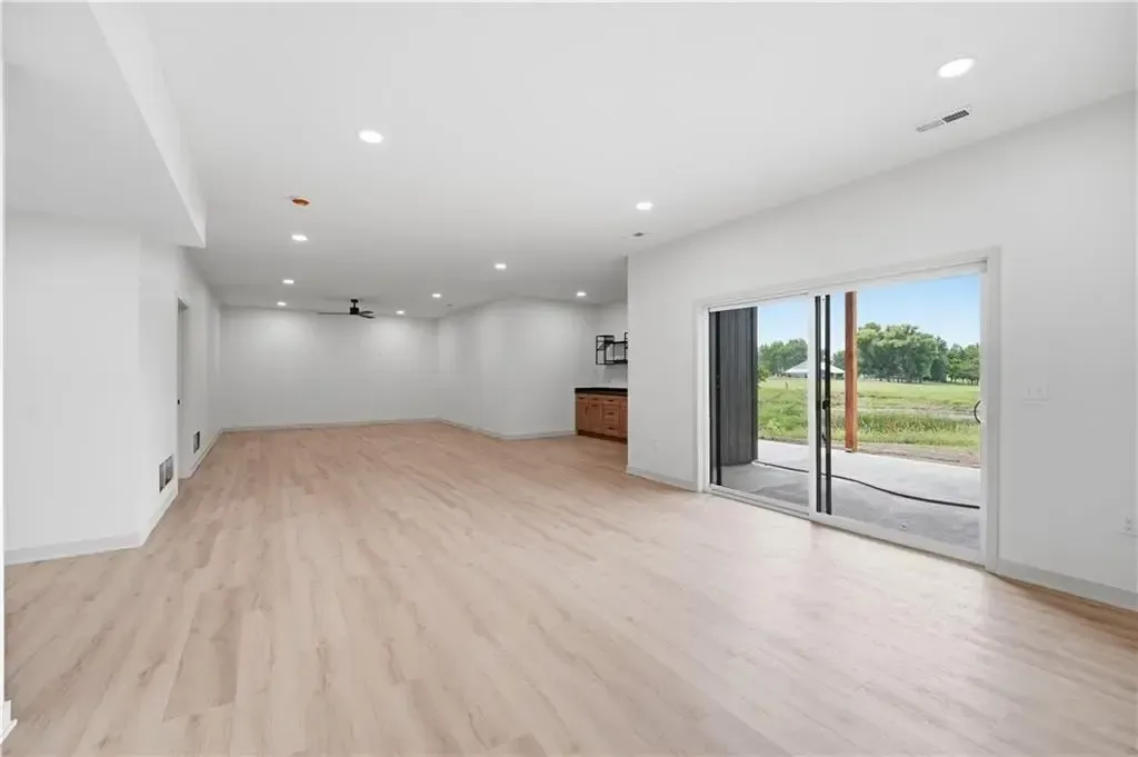 Bright empty modern room with light wood floors, white walls, recessed lights, and sliding glass doors to a patio.