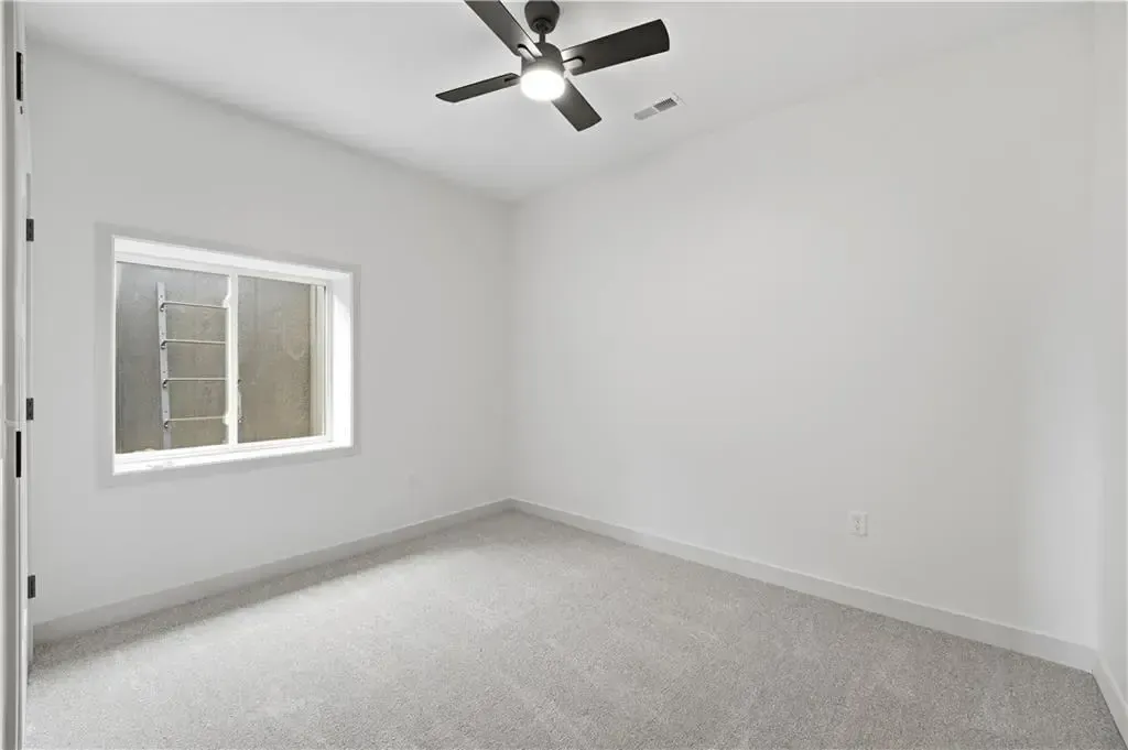 Empty white bedroom with gray carpet, window, and ceiling fan