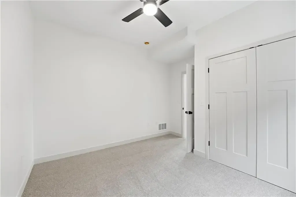 Empty white bedroom with carpet, ceiling fan, and closet doors