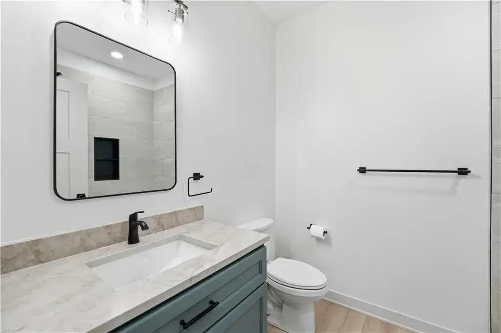 Modern bathroom with white walls, gray vanity, large mirror, toilet, and towel bar.