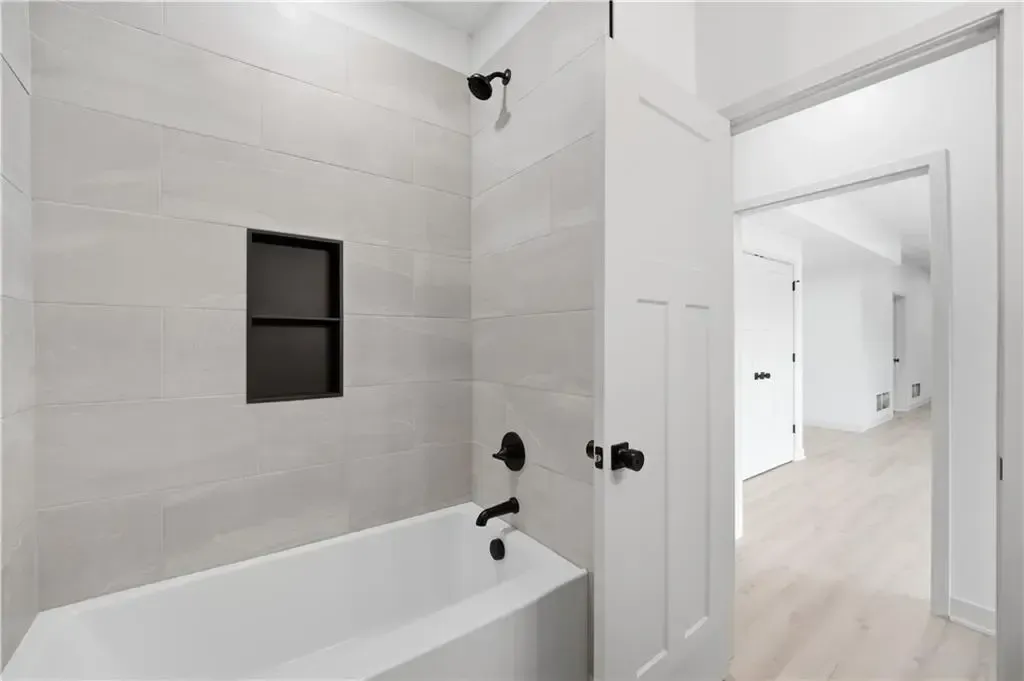 Bright white bathroom with bathtub, black fixtures, and an open doorway to a light hallway