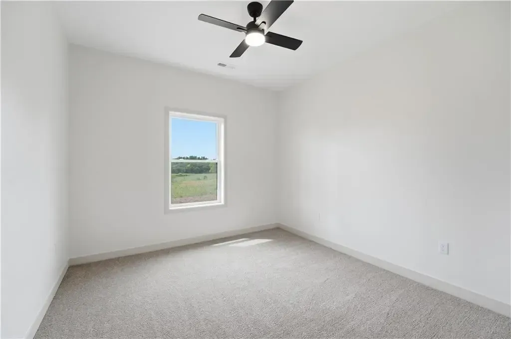 Empty white bedroom with gray carpet, a window, and a ceiling fan