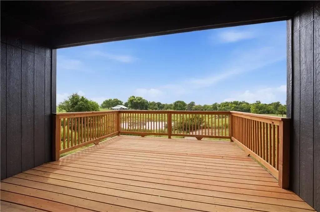 Wooden deck with railing and open view of green trees under a blue sky