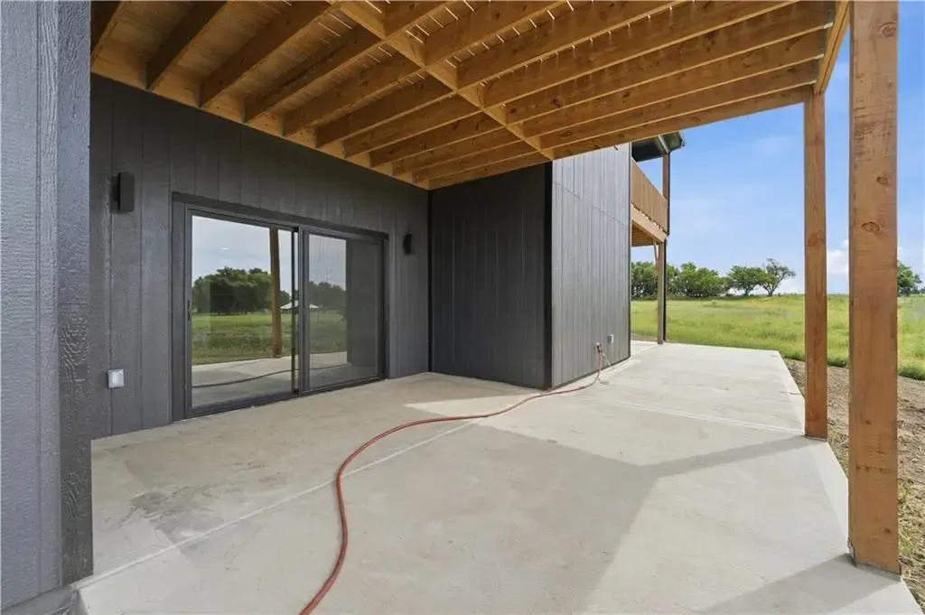 Covered patio with wood ceiling, dark siding, concrete floor, and sliding glass doors overlooking open fields