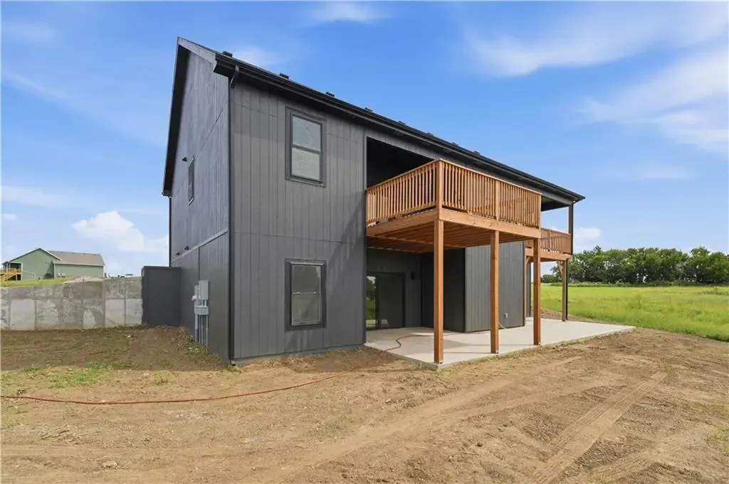 Dark gray two-story house with a wooden balcony on a dirt lot under a blue sky
