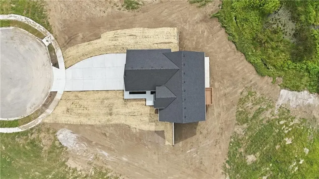 Aerial view of a dark-roofed house beside a curved driveway and dirt yard with a round concrete structure.