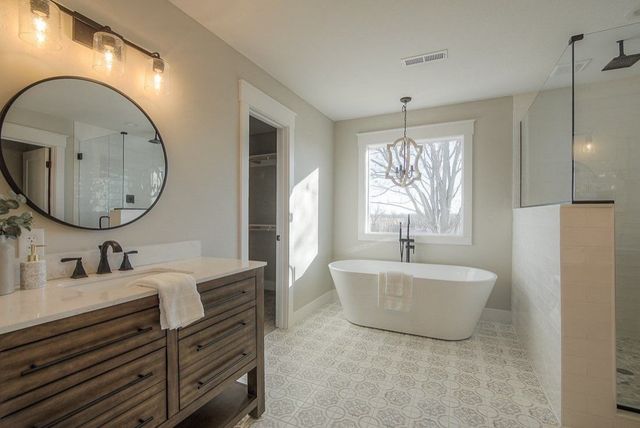 Bright modern bathroom with freestanding tub, double vanity, round mirror, and window view of trees