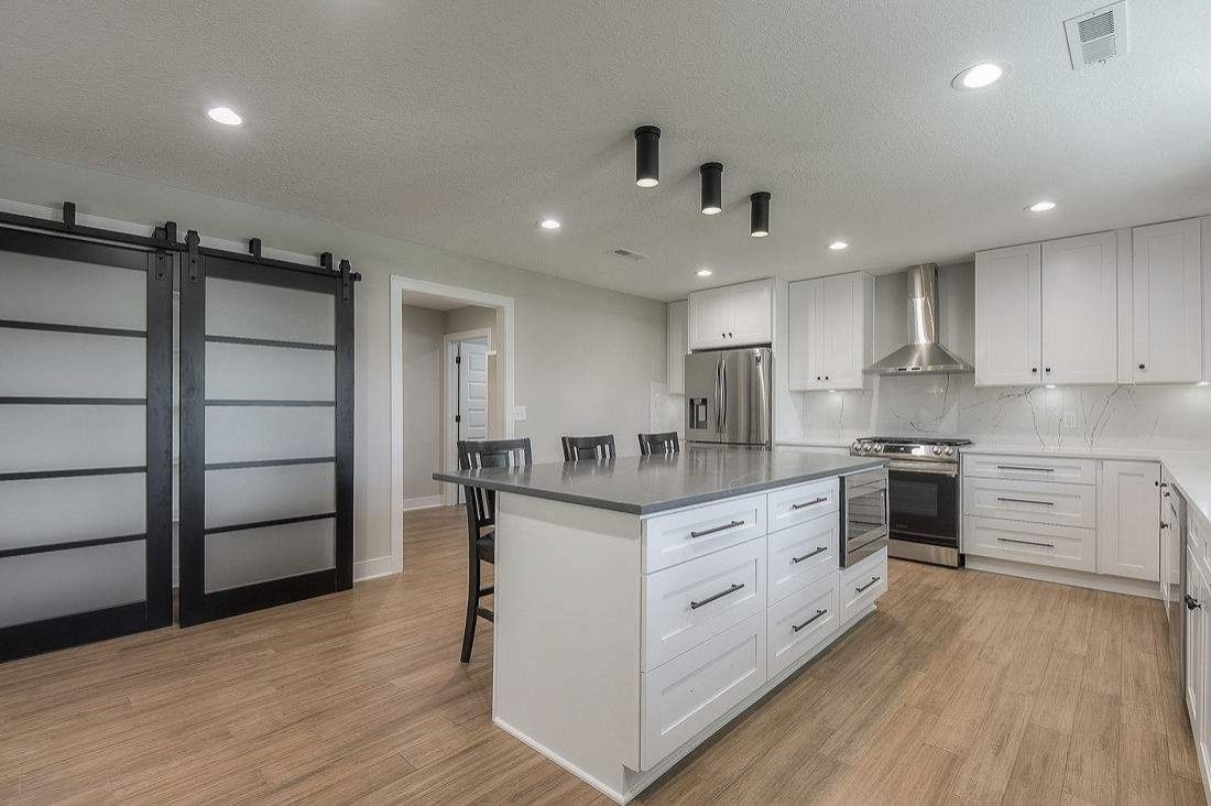 Modern kitchen with white cabinets, island, stainless appliances, and wood floors; black shelving on the left.