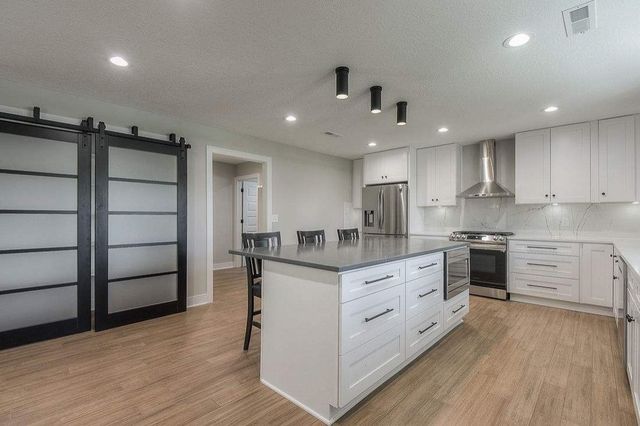 Modern kitchen with white cabinets, stainless appliances, island, wood floors, and black sliding barn door.