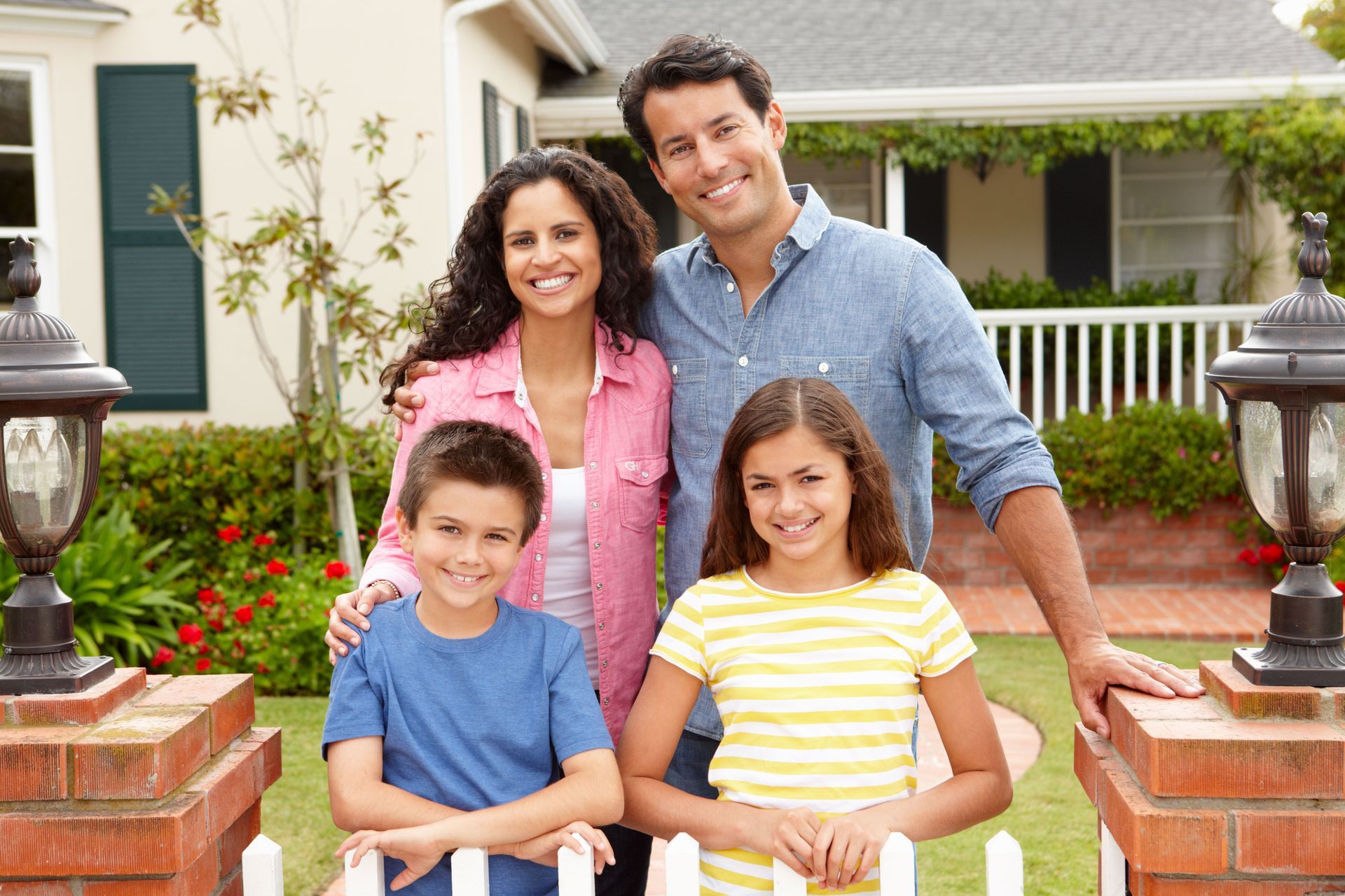 Family of four smiling outside a house, with two children in front and parents behind them.