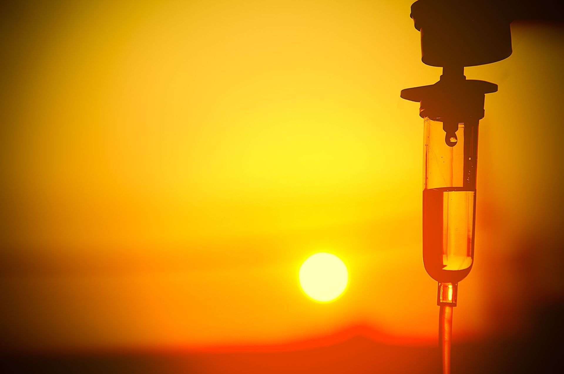 IV bag with dripping solution against a bright yellow and orange sunset.