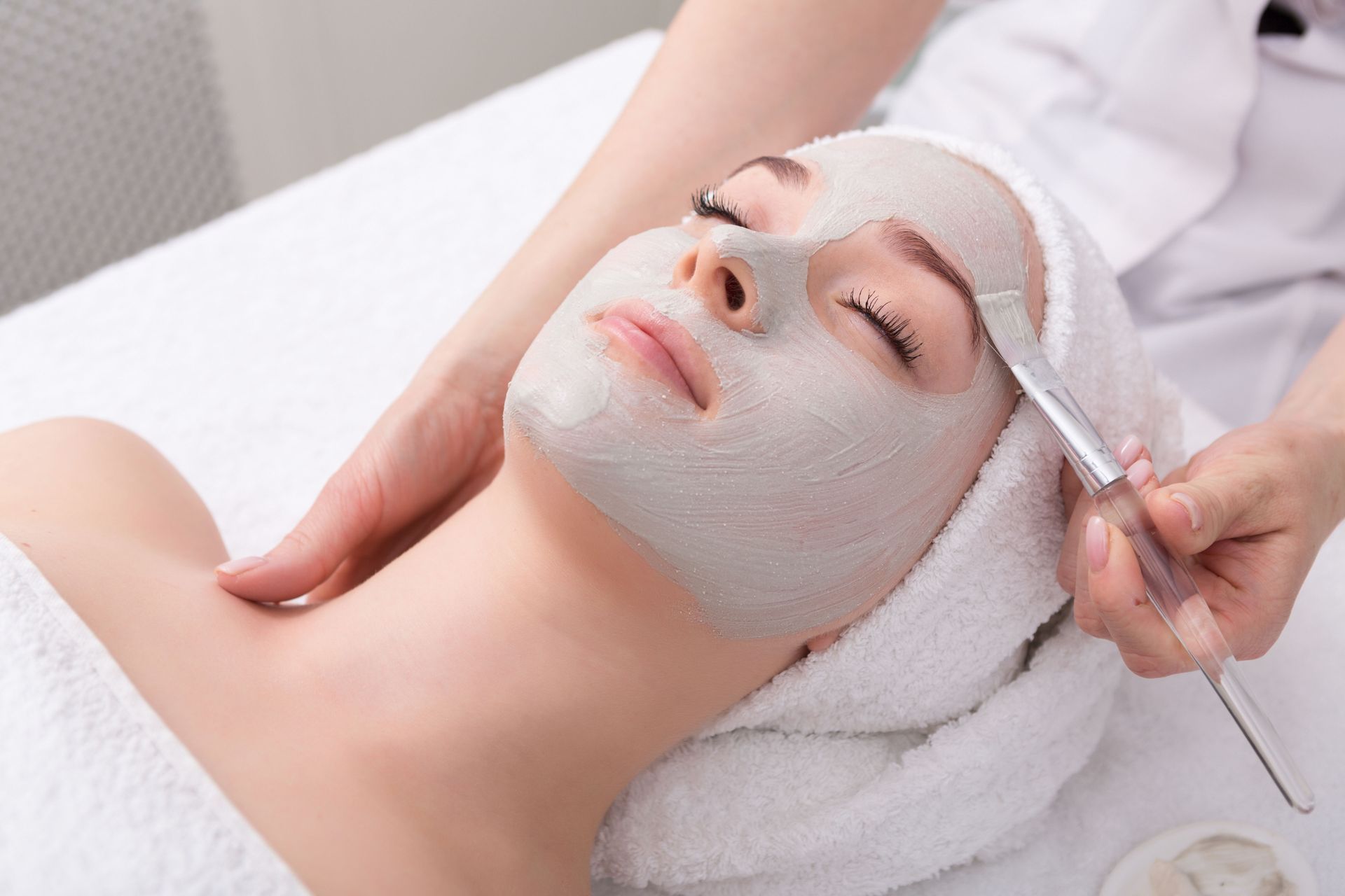 Person receiving a white facial mask treatment while lying on a spa bed