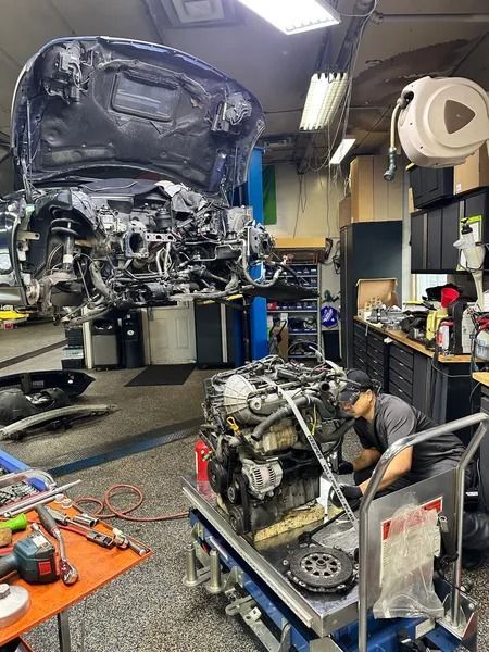 A mechanic works on a car engine removed from a vehicle raised on a lift inside an auto repair shop.