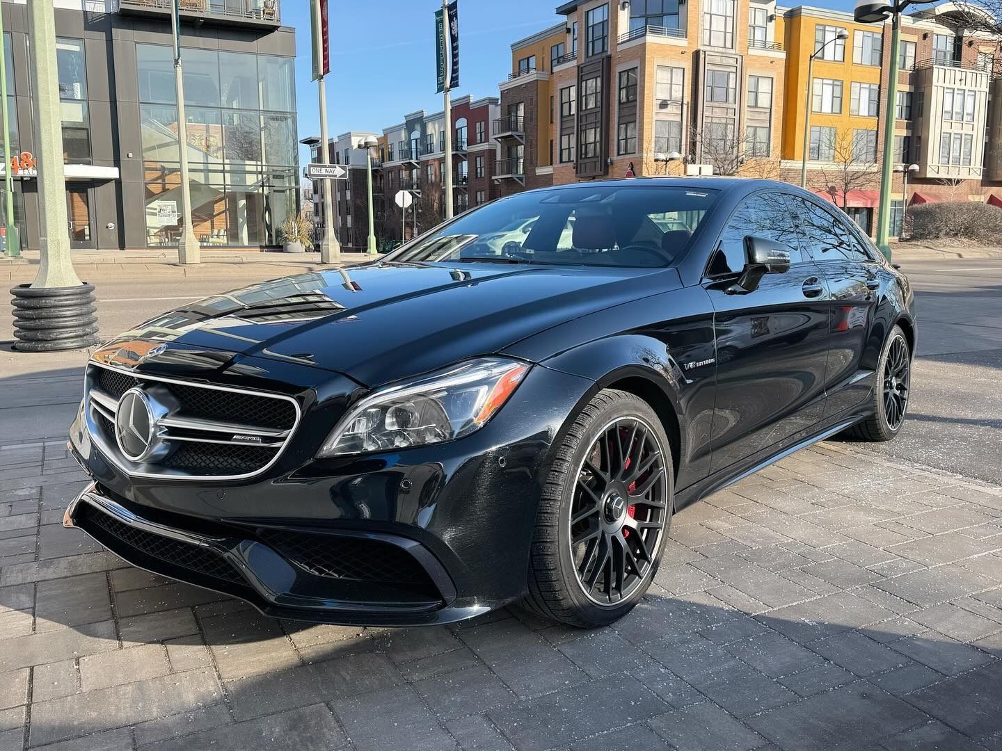 A sleek black Mercedes-Benz sedan parked on a city street during the day with urban buildings in the background.