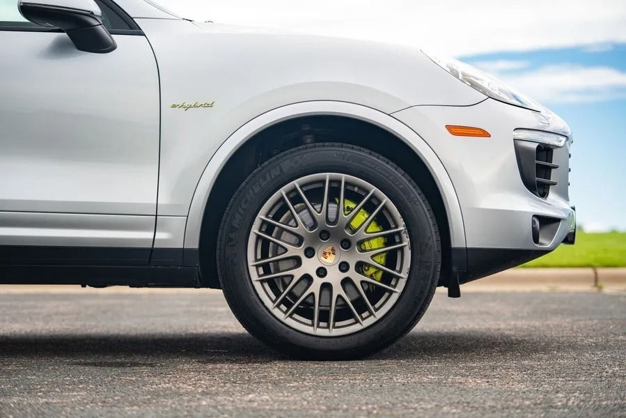 Side view of a silver Porsche SUV with neon green brake calipers and gray multi-spoke wheels on an asphalt road.
