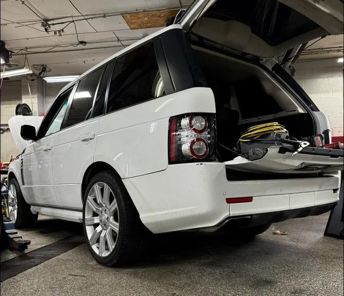 A white Land Rover Range Rover with its rear hatch open, parked inside an automotive repair shop.
